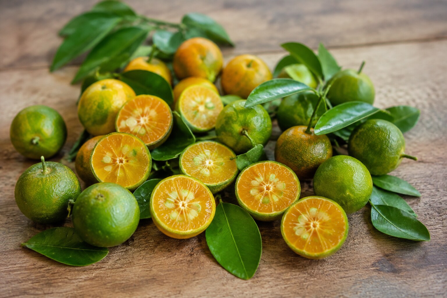 Fresh green and orange calamansi fruits with cut halves showing their juicy segmented interior